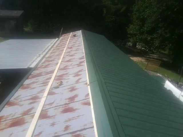 Old rusted panels beside newly installed green metal roofing — Wind Damage Roof Repair by Roofing Brothers in Winnabow