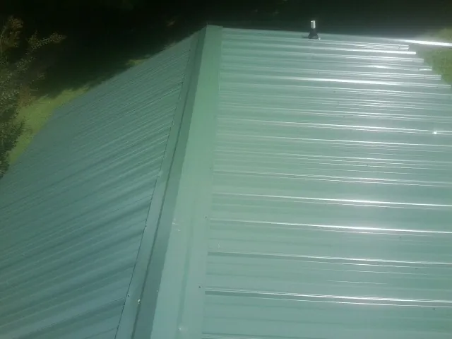 New green metal panels meeting at the ridge of a roof — Flat Roof Repair work by our crew in Winnabow