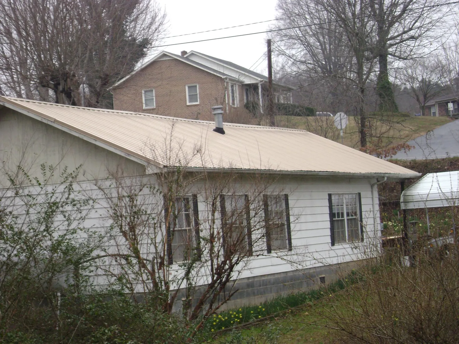 Tan metal roof on a white sided house set into a hillside — Commercial Roofing by Roofing Brothers in Winnabow